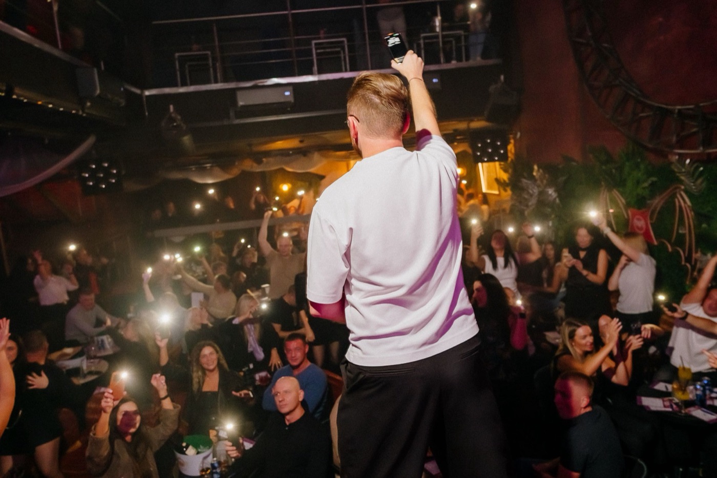 The host on stage raises his phone as the whole room lights up with phone torches